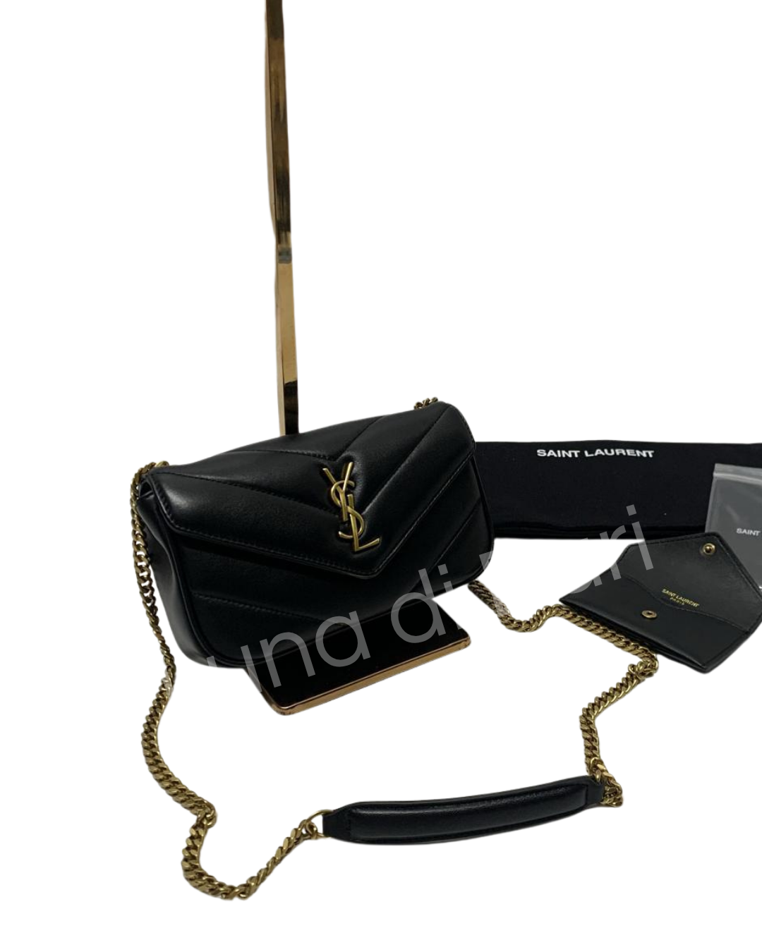 Bolsa Saint Laurent Loulou Toy em couro preto com matelassê chevron, logo e alça de corrente dourados. Detalhe da alça acolchoada e acessórios sobre fundo branco.