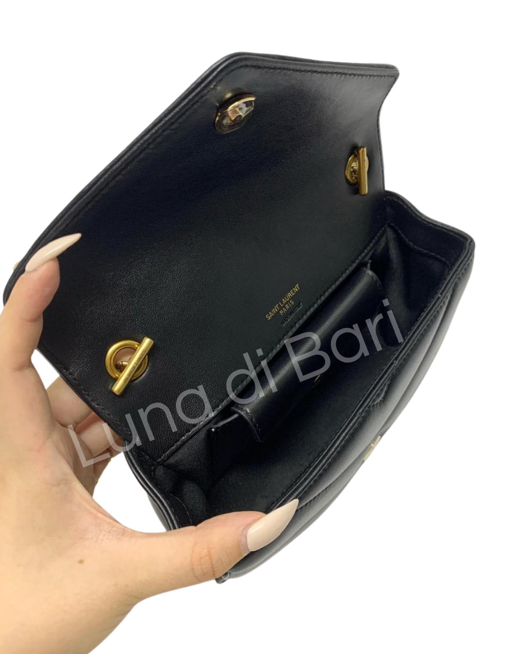 Bolsa Saint Laurent Loulou Toy preta aberta, mostrando o interior forrado em preto com ferragens internas douradas e o logo da marca gravado. Mão segurando a aba.