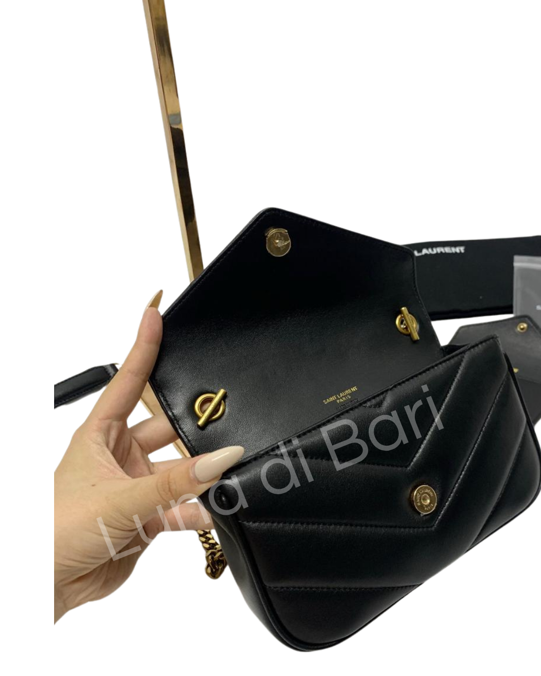 Interior da bolsa Saint Laurent Loulou Toy preta, aberta lateralmente. Detalhe do acabamento em couro, ferragens douradas e compartimento interno. Mão segurando a bolsa.
