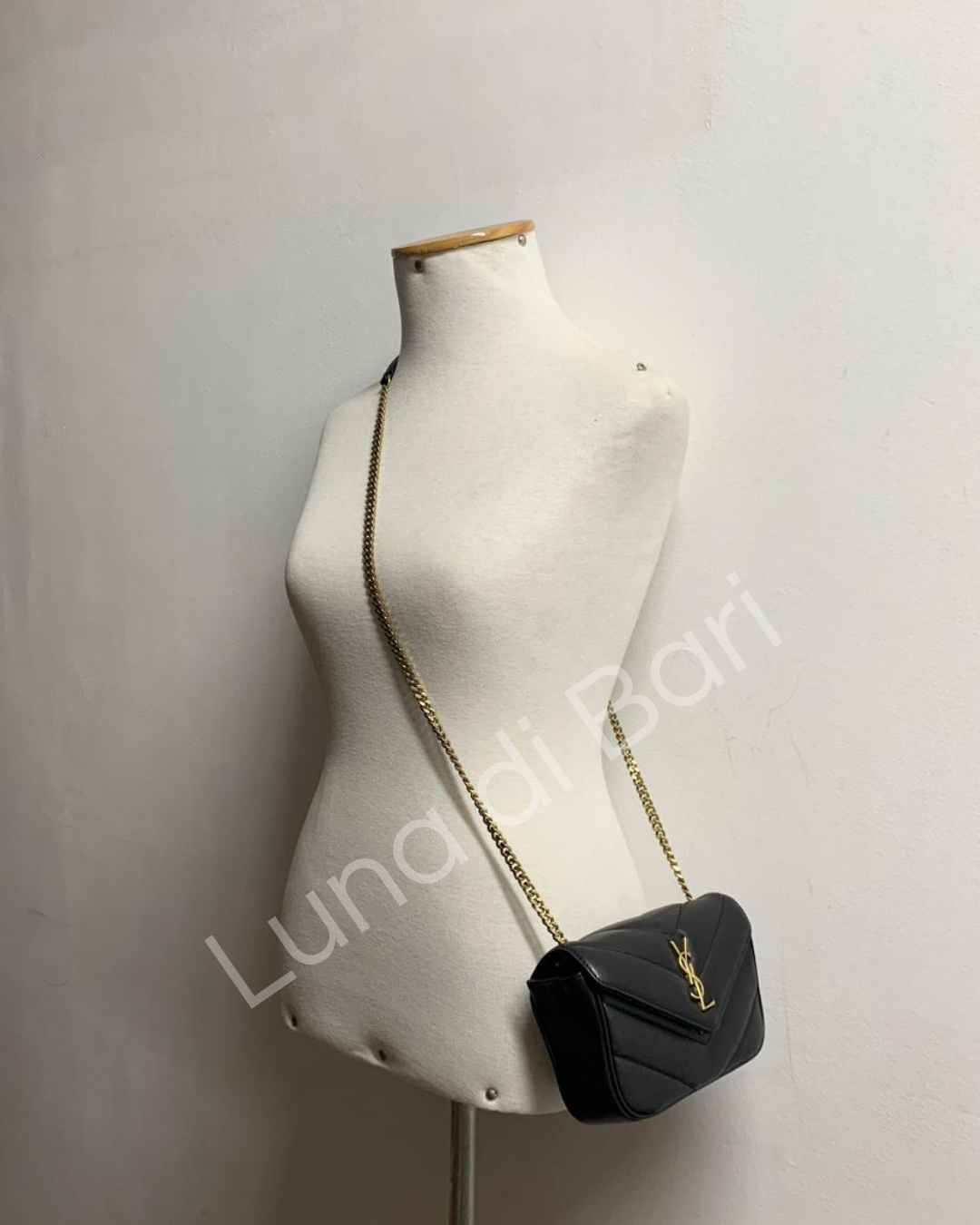 Bolsa Saint Laurent Loulou Toy preta com logo YSL dourado, sendo usada em um manequim. Alça de corrente dourada em comprimento estendido, vista lateralmente.
