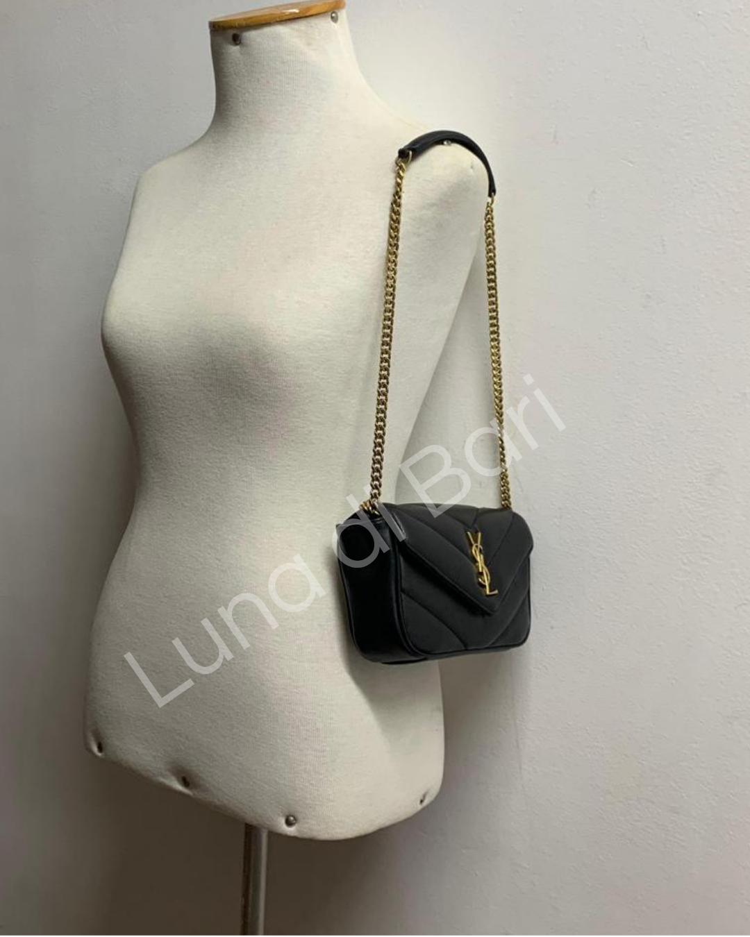 Bolsa Saint Laurent Loulou Toy preta com matelassê em chevron, usada em manequim. Visão traseira da bolsa com a alça de corrente dourada ajustada no ombro.